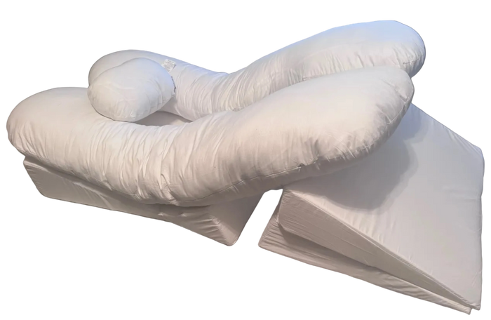 The BBL Add On Set includes a white U-shaped body pillow with an attached cylindrical neck pillow, placed atop two wedge-shaped cushions. All pieces are covered in soft white fabric—ideal for BBL recovery.