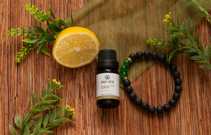 The Bergamot Essential Oil & Diffuser Bracelet set rests on a wooden surface with fresh lemon, green leaves, and sheer cloth—an ideal pairing for your aromatherapy rituals.