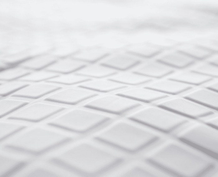 Close-up of the Opulence Glacier Blanket's white surface, featuring a repeating pattern of raised, diamond-shaped tiles that mimic its geometric, textured design. The softly focused image showcases the cooling and weighted qualities for adults.