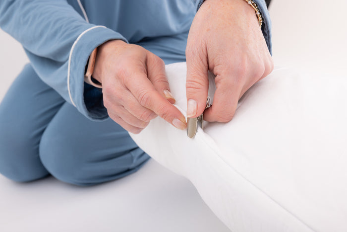 A woman's hand demonstrating attaching the clasp of the strap to the edge of a pillow.