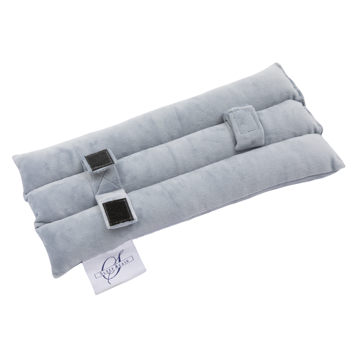 The Seat Belt Pillow is a soft, rectangular, light gray fabric wrap with two fold-over straps and Velcro fastenings, featuring a white logo tag on one end. Ideal for chest support after surgery, it's shown on a white background.