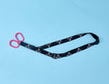 A pair of pink-handled safety scissors attached to a black lanyard with white BABY BOK logos, placed on a light blue background—perfect for use alongside the Surgical Drain Holder.