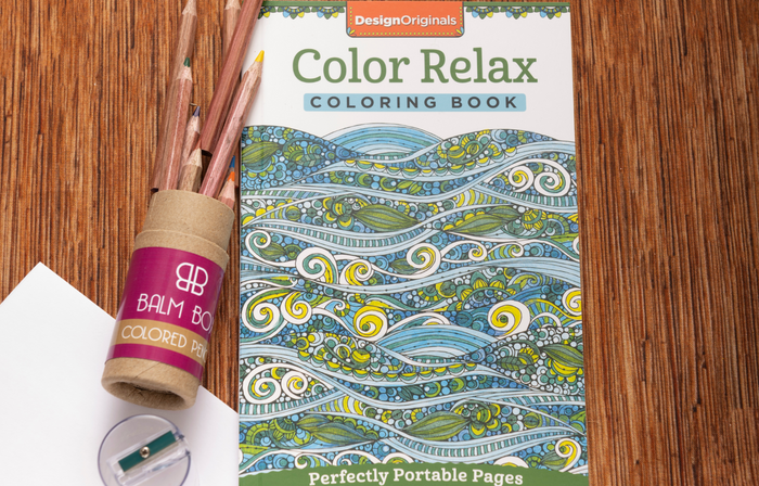 A Color Relax coloring book with a wave design sits by colored pencils and a sharpener—perfect self-care for cancer patients or as a thoughtful gift in the Sweetest Rest & Recovery Box.