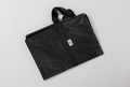 The Travel and Storage Bag for Sleep Again Pillow System is a black, rectangular, water-resistant reusable bag with short handles, folded flat on a white surface. A small white logo label on the front makes it ideal for travel and storage.